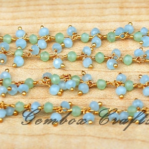 Puede incluir: Una hebra de cadena de oro con cuentas de piedras preciosas de color azul claro y verde. Las cuentas están enhebradas en un patrón en cascada, creando un aspecto delicado y elegante.