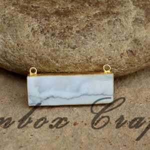 May include: A white marble rectangle pendant with gold-toned metal accents. The pendant has a smooth, polished surface and a subtle marbled pattern.