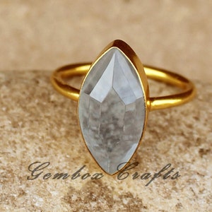 May include: A gold ring with a large, clear, faceted gemstone. The gemstone is a marquise shape and is set in a gold band.