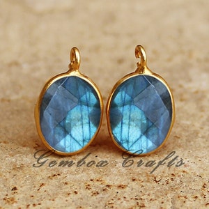 May include: Two gold-toned oval pendants with blue labradorite gemstones. The pendants have a loop at the top for attaching to a chain or cord.