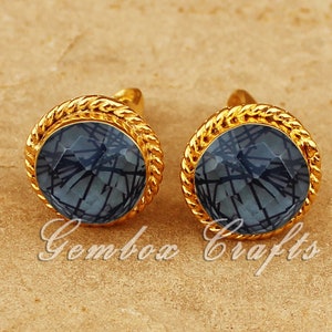 May include: A pair of gold earrings with a blue gemstone in the center. The earrings have a rope-like design around the edge of the gemstone.