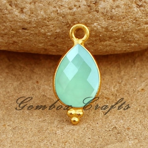 Puede incluir: Pendiente chapado en oro con una piedra preciosa de color azul claro en forma de lágrima. El pendiente tiene un pequeño bucle en la parte superior para sujetarlo a una cadena o cordón.