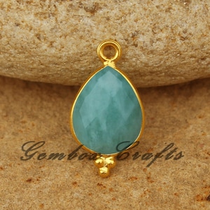 May include: Gold pendant featuring a teardrop-shaped light blue gemstone and three small gold beads.
