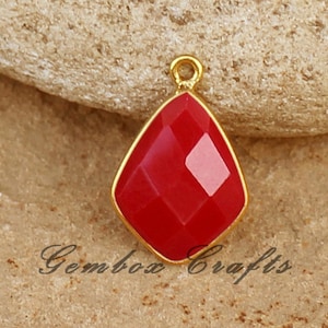 以下が含まれることがあります： 金メッキされたセッティングに赤い宝石のペンダント。宝石はファセットカットされており、ダイヤモンドの形をしています。ペンダントは、どんなジュエリープロジェクトにもエレガントなタッチを加えるのに最適です。