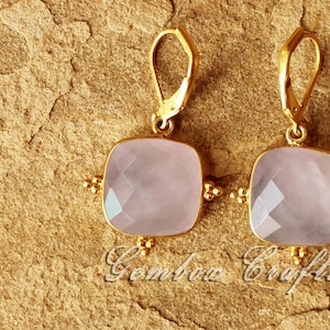 May include: A pair of gold earrings with light pink square-shaped gemstone drops. The earrings have a delicate design with small gold beads around the edges of the gemstones.