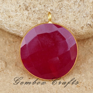 Pode incluir: Um pingente redondo de pedra preciosa vermelha com uma configuração de ouro. A pedra preciosa tem um design facetado e está configurada em um bezel circular.