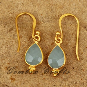 May include: A pair of gold earrings with teardrop-shaped light blue gemstones. The earrings have a simple design and are perfect for everyday wear.