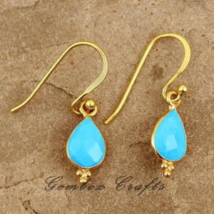 May include: A pair of gold dangle earrings with a teardrop-shaped turquoise blue gemstone. The earrings have a simple design and are perfect for everyday wear.