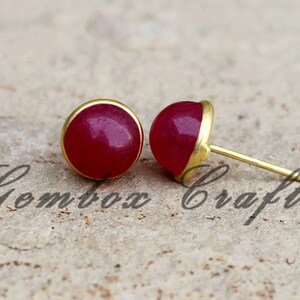 May include: A pair of gold stud earrings with round, red gemstone accents.