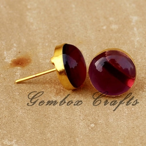 May include: A pair of gold stud earrings with round, purple, translucent stones.