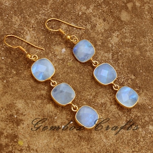 May include: A pair of gold dangle earrings with four light blue moonstone gemstones. Each earring has a teardrop-shaped hook.