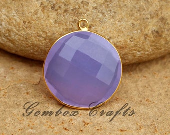 May include: A round, lavender-colored gemstone pendant with a gold-toned bezel setting. The pendant is on a rough, brown stone surface.