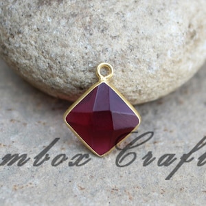 Puede incluir: Un colgante de oro con una piedra preciosa de color rojo oscuro de forma cuadrada y facetada.