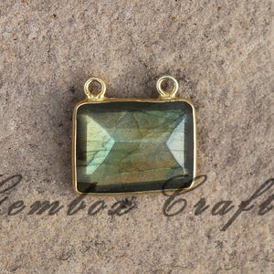 Pode incluir: Pingente dourado com uma pedra preciosa de labradorita de forma quadrada. A pedra preciosa tem um brilho iridescente verde e azul.