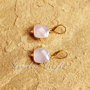 May include: A pair of gold earrings with pink gemstone square drops. The earrings have a simple design with a small loop for hanging.