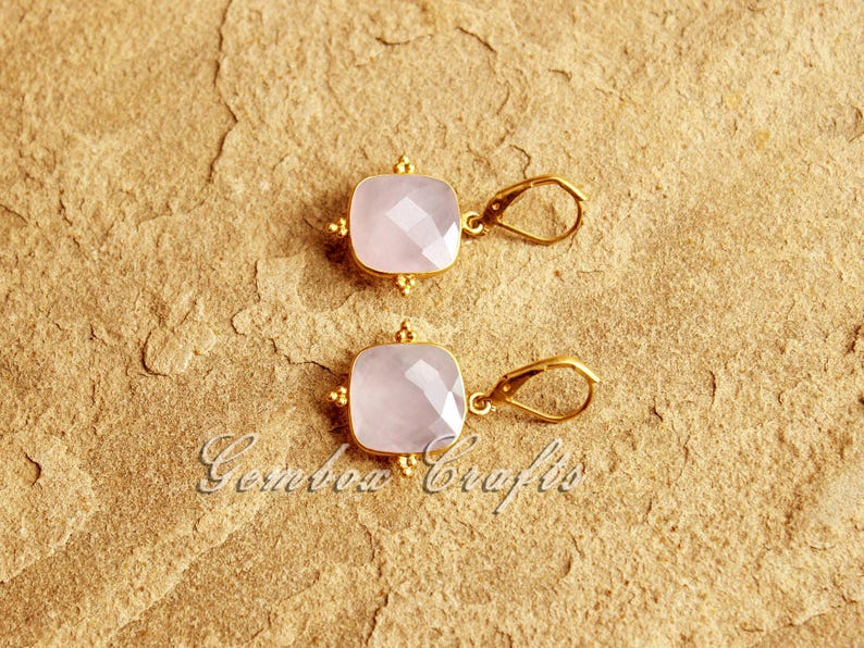 May include: A pair of gold earrings with pink gemstone square drops. The earrings have a simple design with a small loop for hanging.