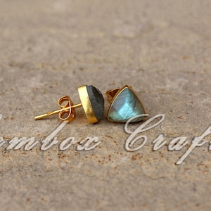 May include: A pair of gold-tone stud earrings featuring triangular labradorite gemstones. The stones have a blue-green iridescent sheen.