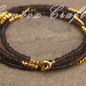 May include: A multi-strand bracelet made with dark grey and gold beads. The bracelet has a gold clasp.