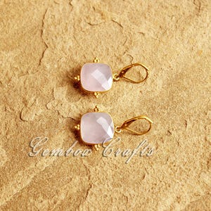 May include: A pair of gold earrings with pink square-shaped gemstones. The earrings have a simple design with a small loop for hanging.