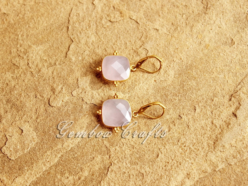 May include: A pair of gold earrings with pink square-shaped gemstones. The earrings have a simple design with a small loop for hanging.