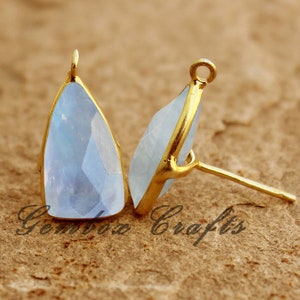 May include: A pair of light blue gemstone earrings with gold-toned settings and posts. The earrings are teardrop shaped and have a faceted finish.