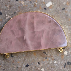 May include: A half-circle pendant made of rose quartz with a gold-toned metal frame and two jump rings.