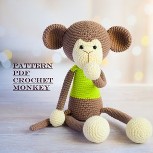 K&ouml;nnte beinhalten: H&auml;kelmuster-PDF f&uuml;r ein braunes und gr&uuml;nes Affen-Amigurumi-Spielzeug. Der Affe sitzt mit den H&auml;nden vor der Brust verschr&auml;nkt. Der Text "PATTERN PDF CROCHET MONKEY" ist im Bild sichtbar.