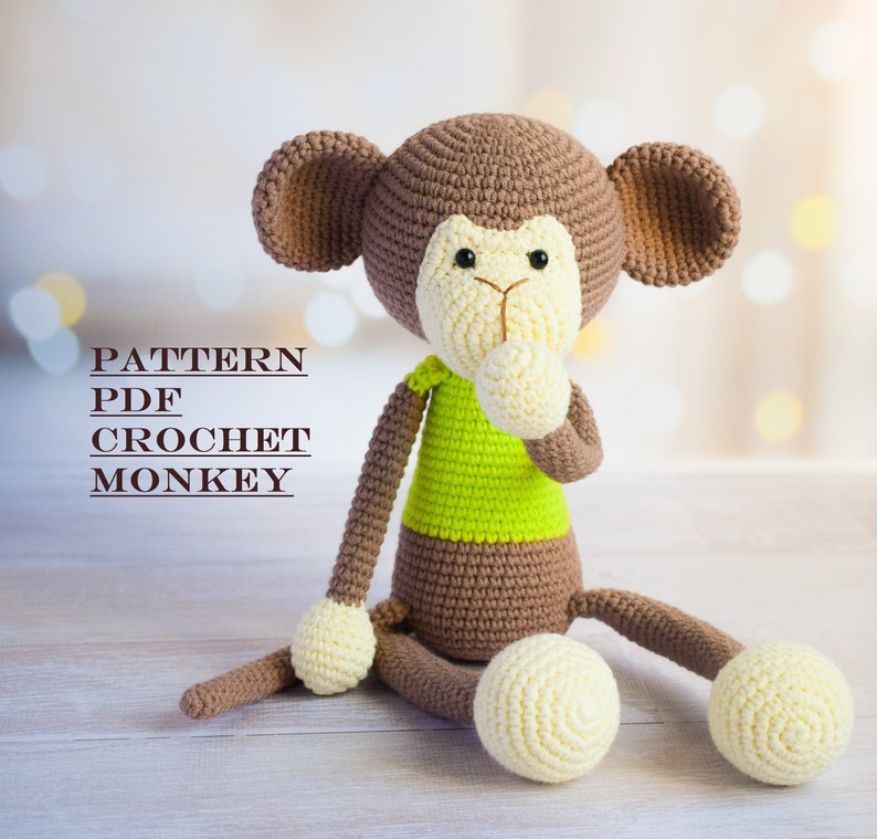K&ouml;nnte beinhalten: H&auml;kelmuster-PDF f&uuml;r ein braunes und gr&uuml;nes Affen-Amigurumi-Spielzeug. Der Affe sitzt mit den H&auml;nden vor der Brust verschr&auml;nkt. Der Text "PATTERN PDF CROCHET MONKEY" ist im Bild sichtbar.