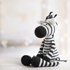 May include: A crocheted zebra stuffed animal with black and white stripes. The zebra is sitting on a white surface.