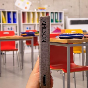 K&ouml;nnte beinhalten: Ein graues Buch mit dem Wort "JAMESON" vertikal auf dem R&uuml;cken gedruckt. Ein Bleistift-Symbol ist unten auf dem R&uuml;cken gedruckt.