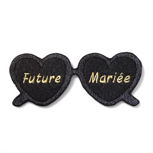 Peut inclure: Lunettes de soleil en forme de cœur en feutre noir avec broderie dorée qui dit "Future" sur une lentille et "Mariée" sur l'autre.