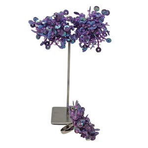 May include: A set of two purple iridescent sequined earrings and a ring. The earrings are attached to a silver stand.