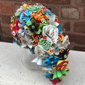 May include: A colorful paper flower bouquet with a variety of colors, including red, blue, green, yellow, and white. The flowers are made from paper and are arranged in a cascading style. The bouquet is perfect for a wedding or other special occasion.