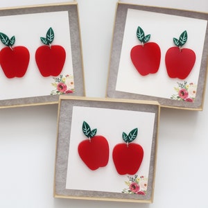 May include: Three small gift boxes each containing a pair of red apple earrings with green leaves. The earrings are made of polymer clay.