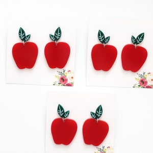 May include: A set of four red apple earrings with green leaves. The earrings are made of acrylic and are perfect for adding a touch of whimsy to any outfit.