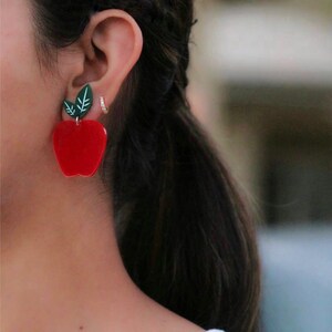 May include: Red apple shaped earrings with green leaves. The earrings are made of acrylic and are a fun and playful accessory.