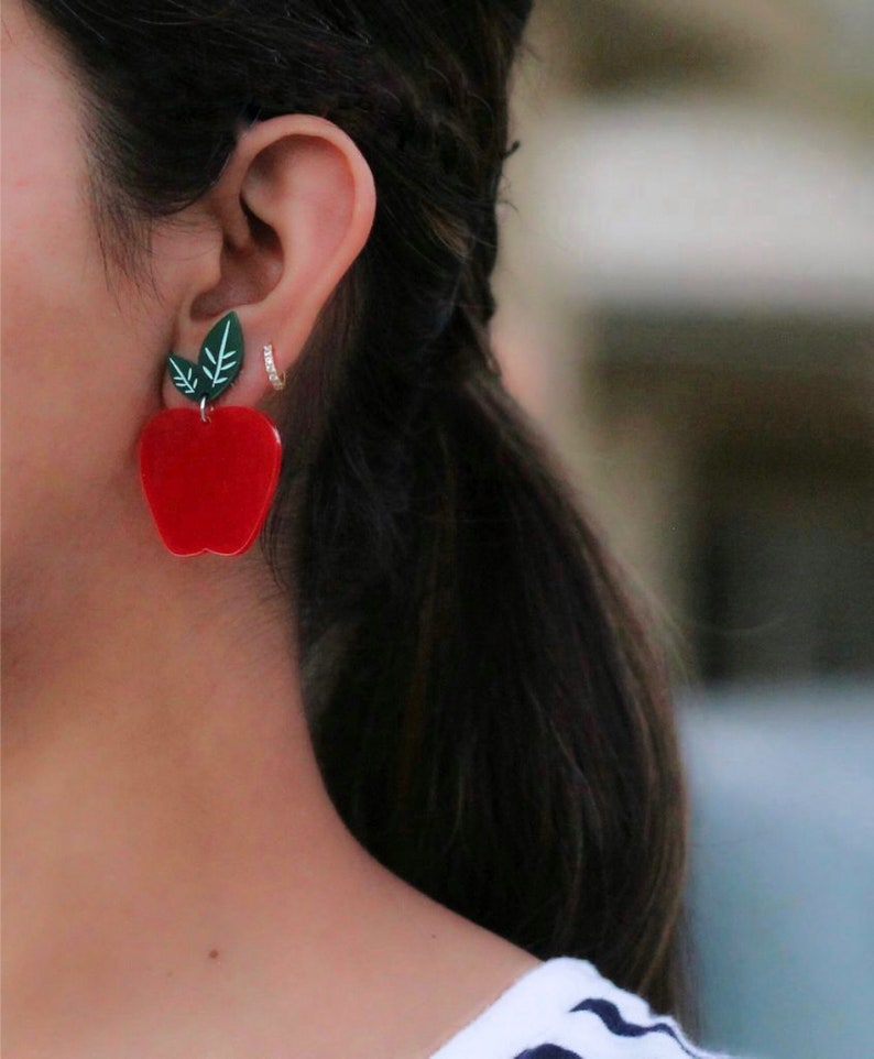 May include: Red apple shaped earrings with green leaves. The earrings are made of acrylic and are a fun and playful accessory.