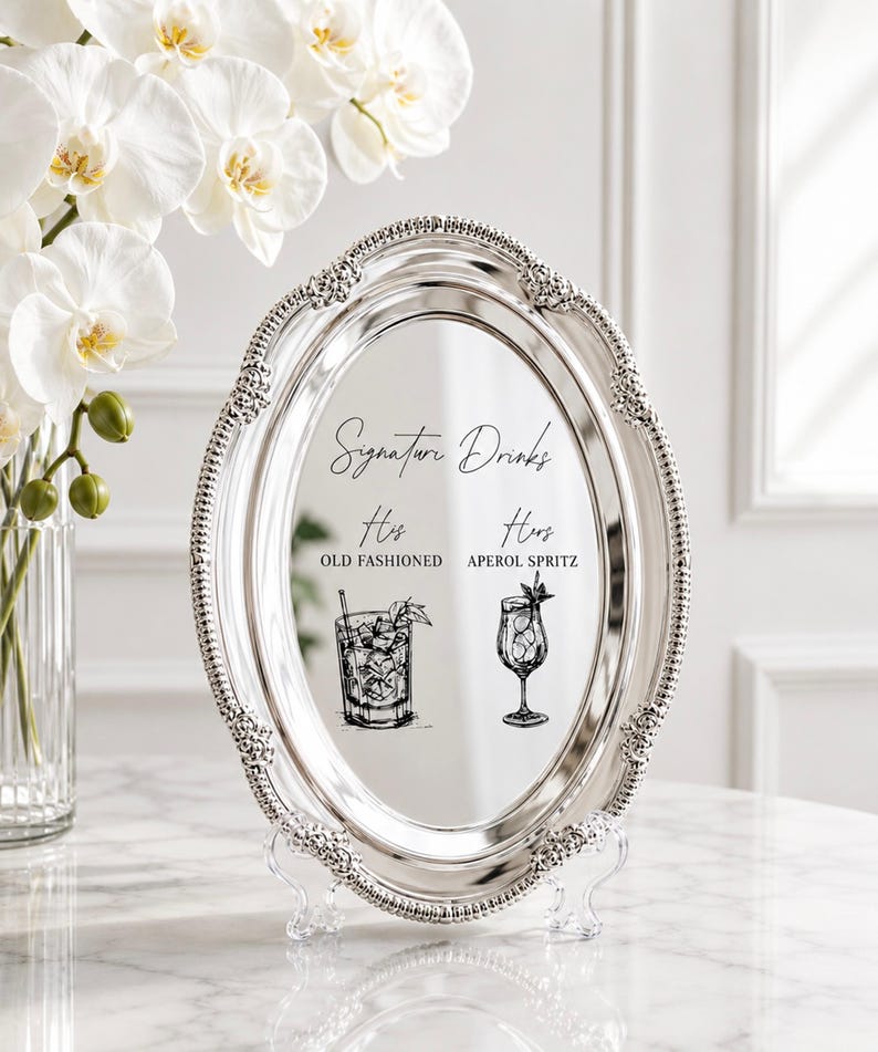 May include: An oval silver-toned mirror tray with a decorative beaded border. The center features black text reading Signature Drinks, His Old Fashioned, and Hers Aperol Spritz, accompanied by black line-art illustrations of an Old Fashioned and a cocktail glass.