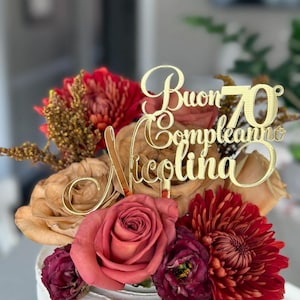 May include: A white cake decorated with red, brown, and burgundy flowers. A gold cake topper says "Buon Compleanno Nicollina 70".