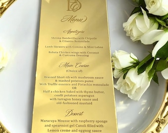 May include: Gold menu card with a black and white design. The menu lists appetizers, main course, and dessert options. The text includes: Shrimp Banderillas with Chipotle & Cilantro Remoulade, Lamb Skewers with Comino & Mint Labne, Robata Chicken wings with Coconut & Curcuma Dressing, Brassed Short rib with mushroom sauce & mashed potatoes puree, Half a chicken baked with thyme butter, confit potatoes asparagus, Maracuya Mousse with raspberry sponge and spearmint gel Canoli filled with Lemon creme and eggnog sauce.