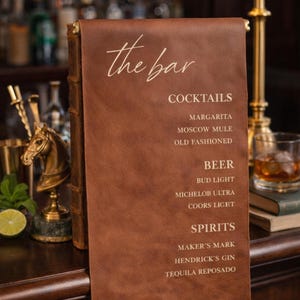 Może przedstawiać: Brązowy skórzany szyld z menu baru z napisem the bar, COCKTAILS, MARGARITA, MOSCOW MULE, OLD FASHIONED, BEER, BUD LIGHT, MICHELOB ULTRA, COORS LIGET, SPIRITS, MAKER'S MARK, HENDRICK'S GIN oraz TEQUILA REPOSADO jasnymi literami.