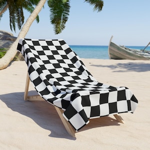 Op de afbeelding: Een zwart-wit geblokte strandstoel met een houten frame. De stoel staat op een zandstrand met palmbomen op de achtergrond.