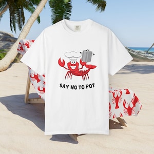 May include: White t-shirt featuring a red cartoon lobster wearing a chef's hat and holding a pot. The text "SAY NO TO POT" is printed below the lobster.
