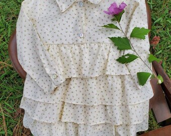 May include: A white dress with a green floral print and a ruffled skirt. The dress has a button-up collar and long sleeves.