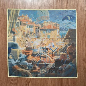 May include: A square handkerchief with a detailed illustration of a European village scene. The artwork features buildings with red tile roofs, blue accents, and a night sky with celestial elements. The handkerchief has a yellow border.