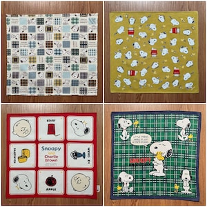 Puede incluir: Cuatro cuadrados de tela diferentes con un perro de dibujos animados con la nariz roja y el pico amarillo. Los cuadrados son todos de diferentes colores y patrones. Un cuadrado es rojo con texto blanco que dice "Snoopy y Charlie Brown". Otro cuadrado es verde con un patrón de cuadros y texto blanco que dice "Snoopy Woodstock".
