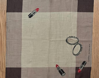 May include: Square handkerchief with a brown, tan, and beige color block design. The handkerchief features illustrations of lipstick tubes and compact mirrors. The text "L'objet pour beaute et fantaisie" is printed on the bottom.