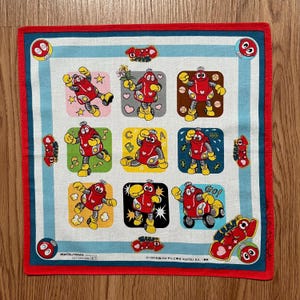 Puede incluir: Un pañuelo de algodón blanco con borde rojo y un patrón repetido de un robot rojo con un corazón en el pecho. El robot está en diferentes poses y tiene diferentes expresiones. El pañuelo tiene el texto "MATSUYAMA" y "©1999年アガツマ ©2000 AGATSU DX.  " impreso en él.