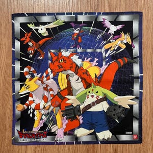 Peut inclure: Carré de tissu Digimon avec des personnages de dessins animés colorés sur fond noir et bleu. Les personnages sont dans diverses poses, avec un mélange de teintes rouges, jaunes, vertes et violettes. Le tissu a une bordure argentée.