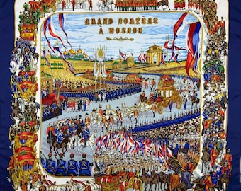 May include: A navy blue silk scarf with a detailed illustration of a parade in Moscow. The design features horse-drawn carriages, soldiers, and architectural elements, framed by a white border. Text in French is visible.